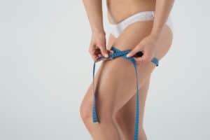 Woman measuring her thigh after thigh lift surgery in Albania.