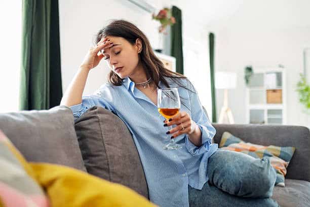 Woman with headache holding glass of wine, health concerns, lifestyle impact.