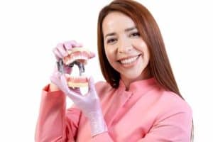 Woman holding dental implant model showcasing All-on-4 and All-on-6 solutions.